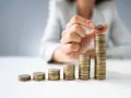 Dłoń układa monety w rosnące słupki, symbolizując wzrost wartości. To wizualizacja zarządzania finansami i optymalizacji faktoring kosztów.