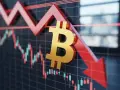 Złoty symbol bitcoin spada wraz z wykresem świecowym, wskazując na spadki wartości. W tle widać odbicie okien, sugerujące biuro.