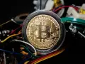 Złoty Bitcoin w otoczeniu kabli i elektroniki, symbolizujący darmowe kopanie kryptowalut.
