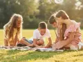 Cztery dzieci rysuje na kocu w parku. To świetny przykład, jak można spędzić czas na świeżym powietrzu.
