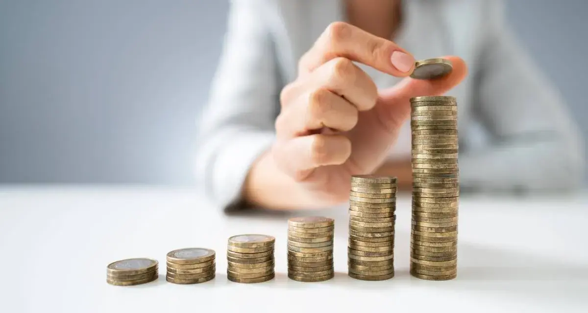 Dłoń układa monety w rosnące słupki, symbolizując wzrost wartości. To wizualizacja zarządzania finansami i optymalizacji faktoring kosztów.