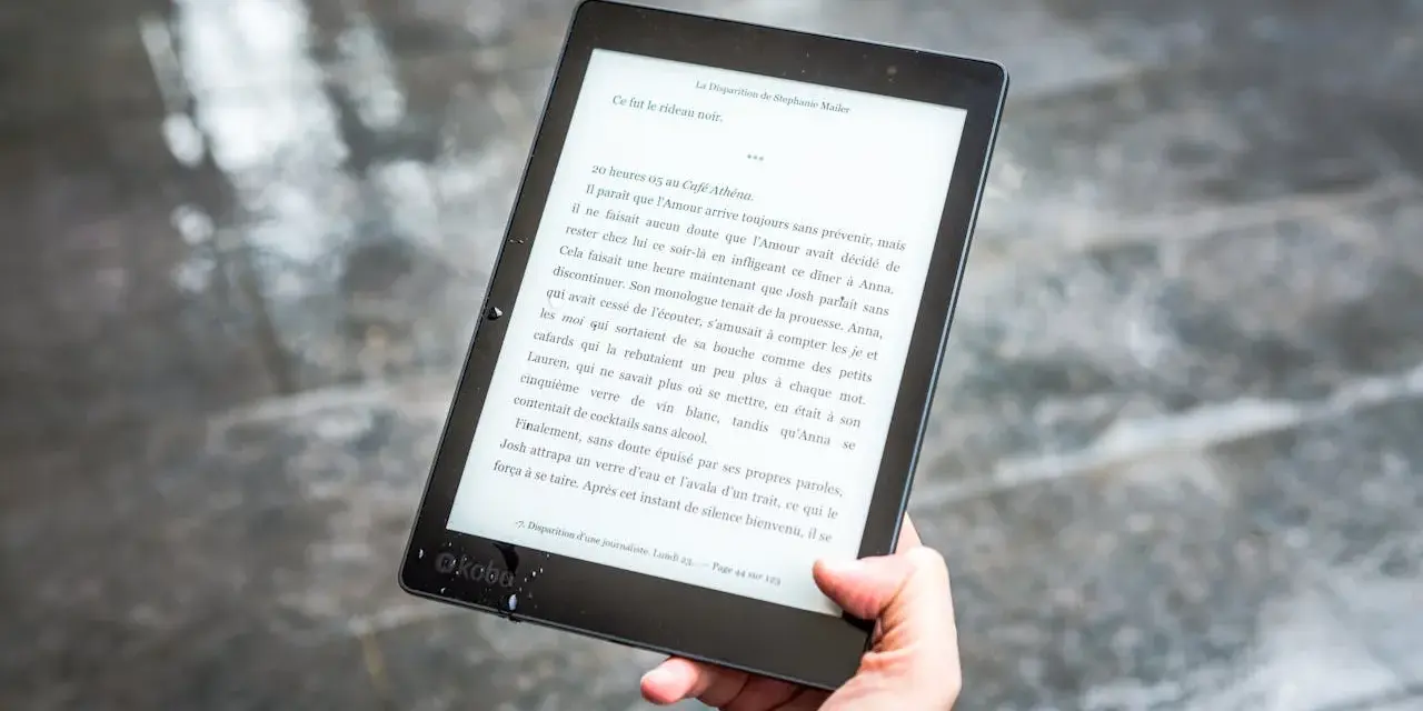 Ręka trzyma czytnik ebooków z tekstem. Czytanie książek elektronicznych to przyjemność, a teraz dzięki zmianom w prawie, vat na ebooki jest korzystniejszy.