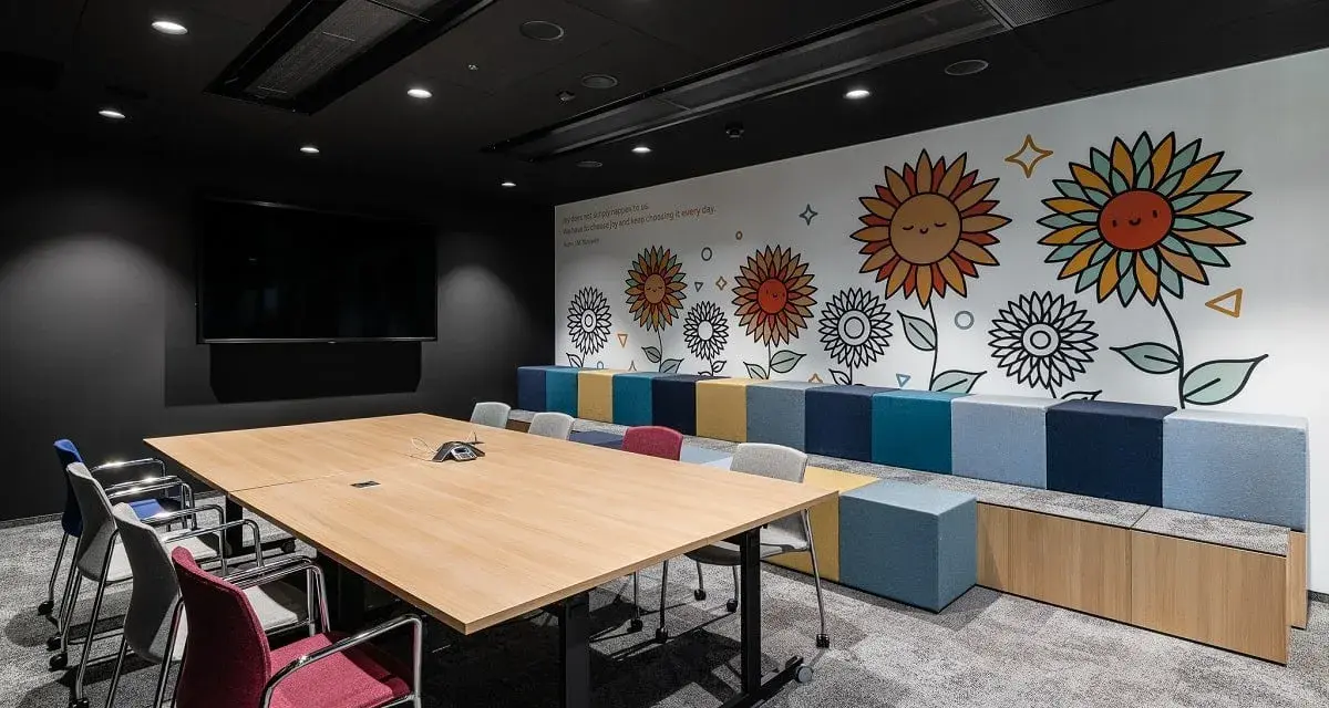 Nowoczesny trading room z dużym stołem, krzesłami i kolorową ścianą z motywem słoneczników.