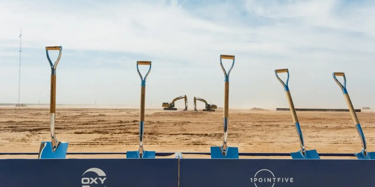 Symboliczne łopaty na placu budowy, gdzie Occidental Petroleum (OXY) rozpoczyna nowy projekt. W tle koparki i wieża.