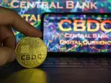 Złoty żeton z napisem CBDC w dłoni, na tle ekranu z wykresem i napisem "CENTRAL BANK DIGITAL CURRENCY". Potencjalne zagrożenia CBDC.