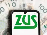 Smartfon z logo ZUS na tle banknotów 100 zł. Informacja o ulgach dla młodych przedsiębiorców, którzy prowadzą działalność gospodarczą do 26 roku życia, zus.