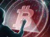 Osoba w kapturze dotyka symbolu Bitcoina na tle kodu binarnego. Czy to ślad po majątku Satoshi Nakamoto?
