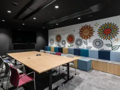 Nowoczesny trading room z dużym stołem, krzesłami i kolorową ścianą z motywem słoneczników.