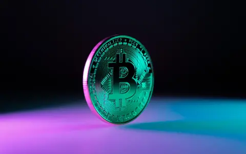 Błyszczący, zielony bitcoin na tle fioletowo-niebieskiego światła. Symbolizuje przyszłość finansów i potencjalny wzrost wartości bit usd.