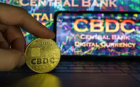 Złoty żeton z napisem CBDC w dłoni, na tle ekranu z wykresem i napisem "CENTRAL BANK DIGITAL CURRENCY". Potencjalne zagrożenia CBDC.