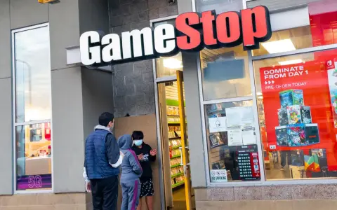Przed sklepem GameStop akcje, ludzie w maskach rozmawiają. W witrynie gry i reklama "DOMINATE FROM DAY 1".
