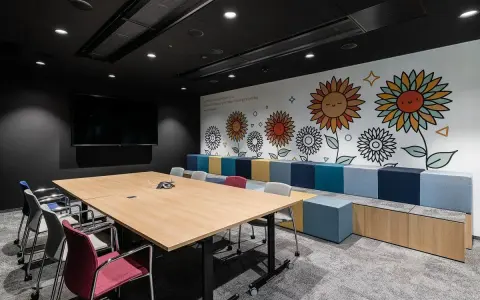 Nowoczesny trading room z dużym stołem, krzesłami i kolorową ścianą z motywem słoneczników.