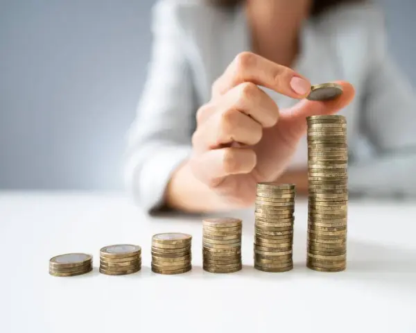 Dłoń układa monety w rosnące słupki, symbolizując wzrost wartości. To wizualizacja zarządzania finansami i optymalizacji faktoring kosztów.