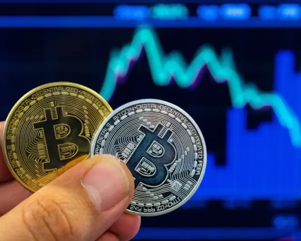 Złoty i srebrny bitcoin w dłoni na tle wykresu giełdowego. Symbolizuje to bitcoin revolution i przyszłość finansów.