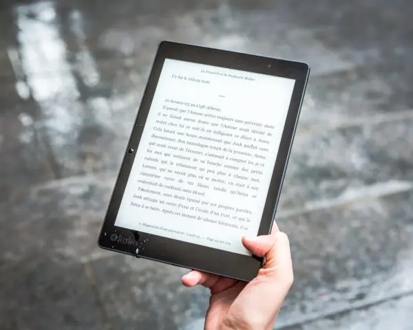 Ręka trzyma czytnik ebooków z tekstem. Czytanie książek elektronicznych to przyjemność, a teraz dzięki zmianom w prawie, vat na ebooki jest korzystniejszy.