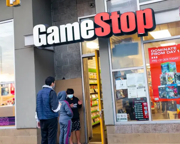 Przed sklepem GameStop akcje, ludzie w maskach rozmawiają. W witrynie gry i reklama "DOMINATE FROM DAY 1".