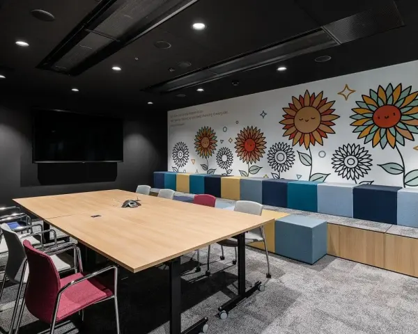 Nowoczesny trading room z dużym stołem, krzesłami i kolorową ścianą z motywem słoneczników.