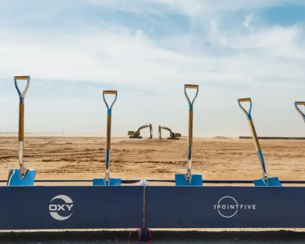 Symboliczne łopaty na placu budowy, gdzie Occidental Petroleum (OXY) rozpoczyna nowy projekt. W tle koparki i wieża.