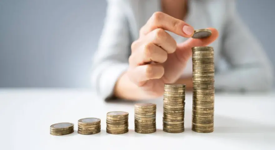 Dłoń układa monety w rosnące słupki, symbolizując wzrost wartości. To wizualizacja zarządzania finansami i optymalizacji faktoring kosztów.