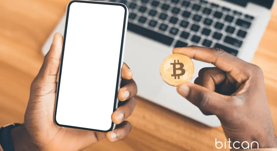Dłoń trzyma smartfon z pustym ekranem i monetę bitcoin. Możliwe, że to początek przygody z kopanie kryptowalut na telefonie.
