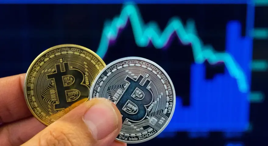 Złoty i srebrny bitcoin w dłoni na tle wykresu giełdowego. Symbolizuje to bitcoin revolution i przyszłość finansów.