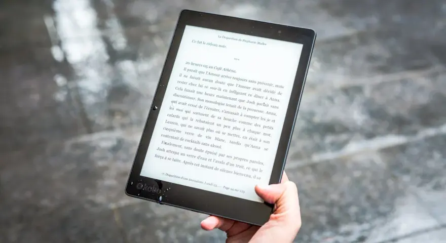 Ręka trzyma czytnik ebooków z tekstem. Czytanie książek elektronicznych to przyjemność, a teraz dzięki zmianom w prawie, vat na ebooki jest korzystniejszy.