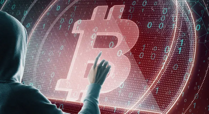 Osoba w kapturze dotyka symbolu Bitcoina na tle kodu binarnego. Czy to ślad po majątku Satoshi Nakamoto?
