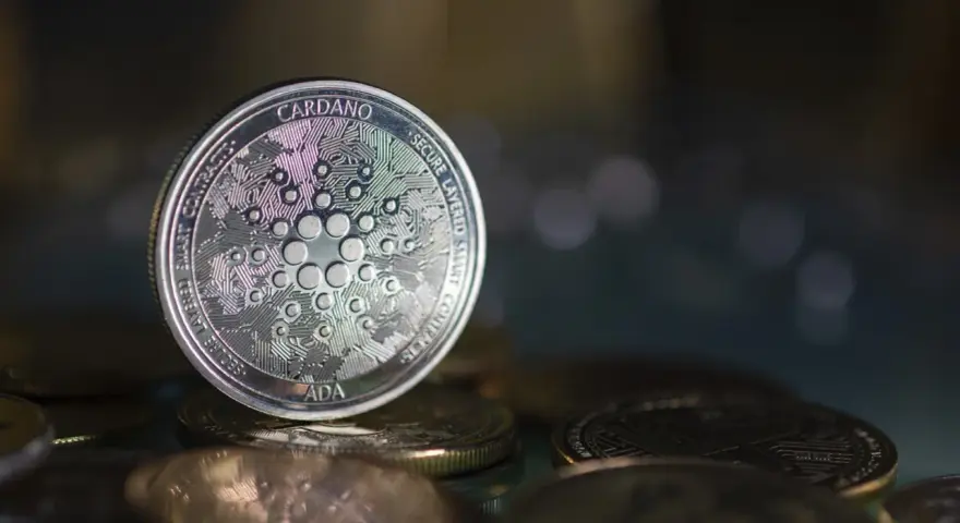 Moneta Cardano (ADA) na stosie innych monet. W tle rozmyte światła, sugerujące analizę i prognozy dotyczące przyszłości kryptowaluty.