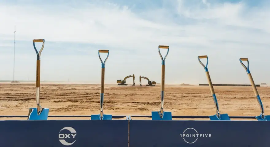 Symboliczne łopaty na placu budowy, gdzie Occidental Petroleum (OXY) rozpoczyna nowy projekt. W tle koparki i wieża.