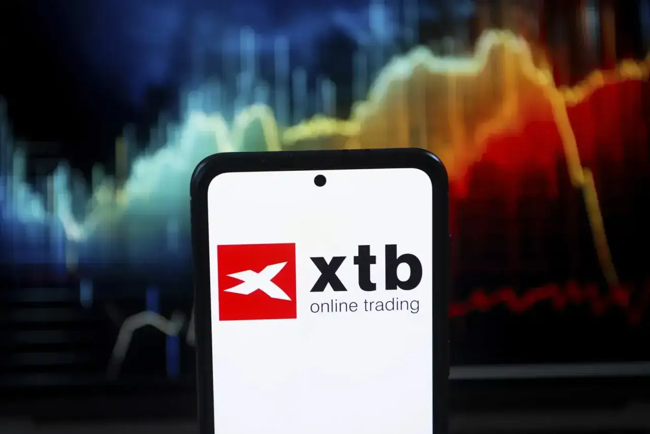 Telefon z logo XTB online trading na tle wykresu giełdowego.